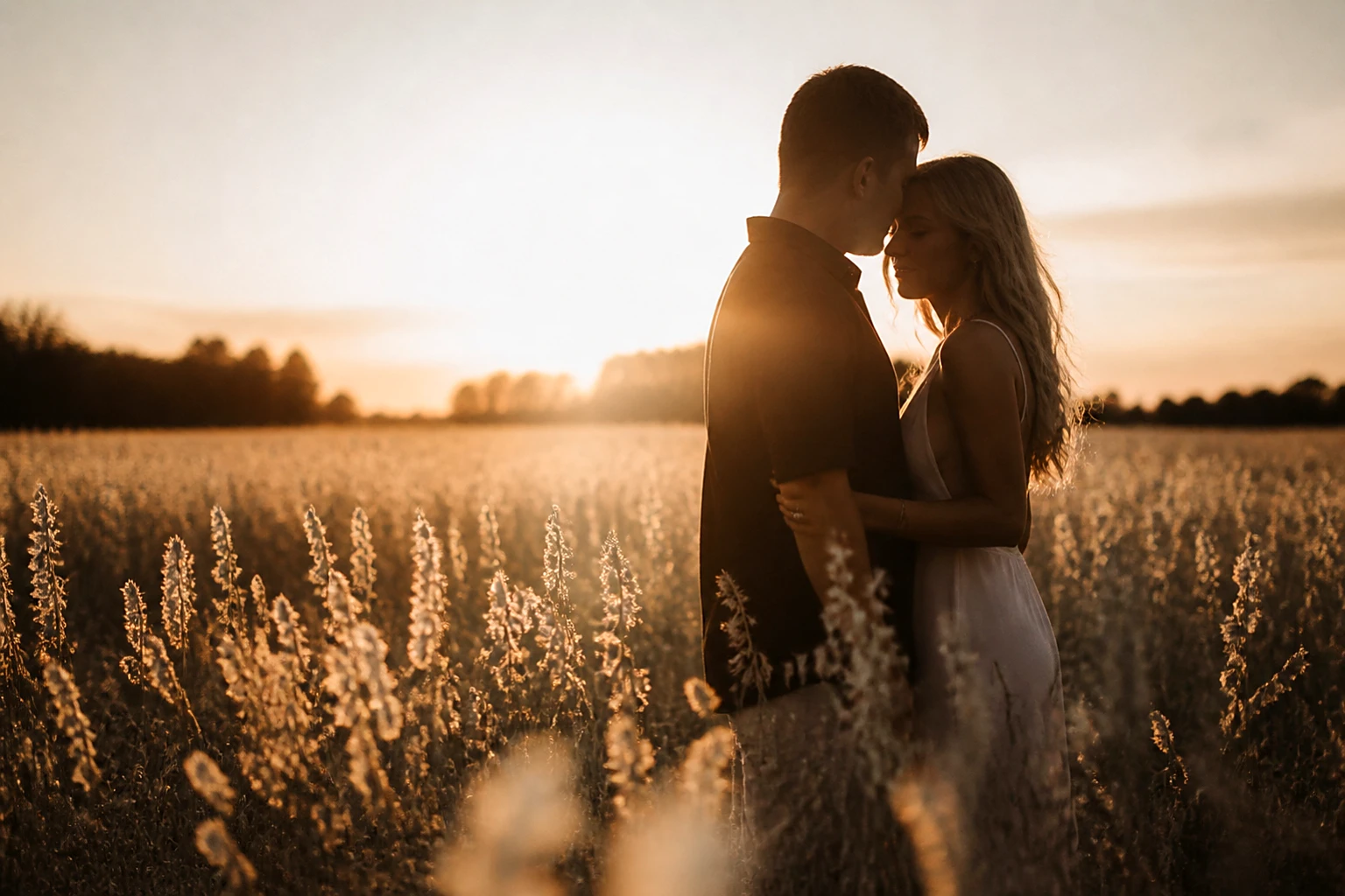 An engaged couple silhouetted against a wide field of pale wheat at sunset